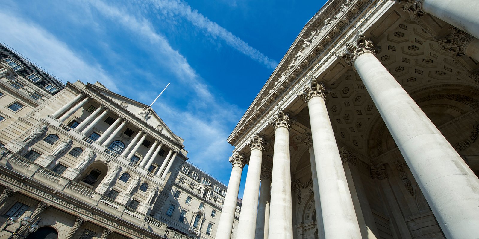 Sunny view of the facade of the Bank of England building and historic Royal Exchange under bright blue sky in The City financial centre of London, UK