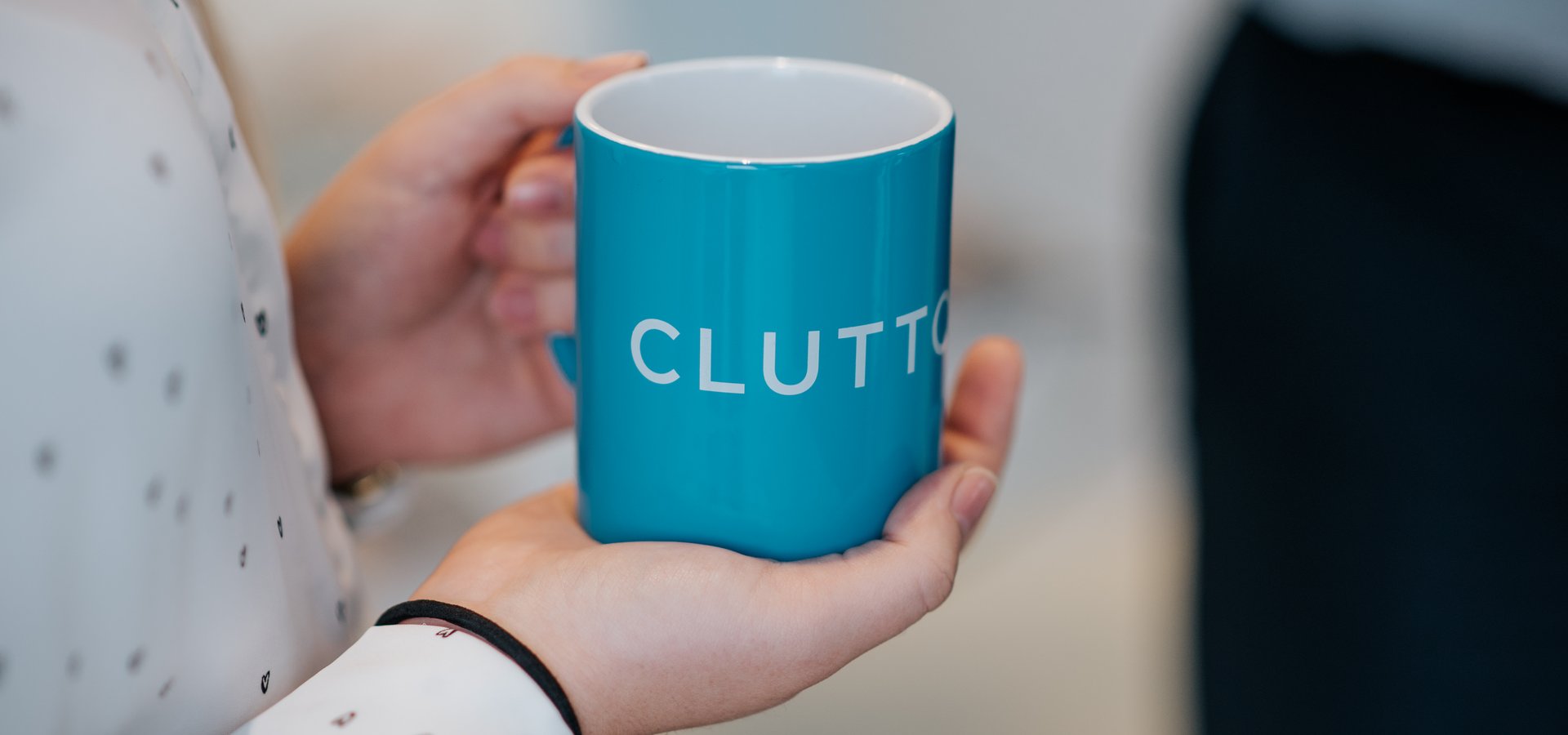 Person holding a Cluttons coffee mug
